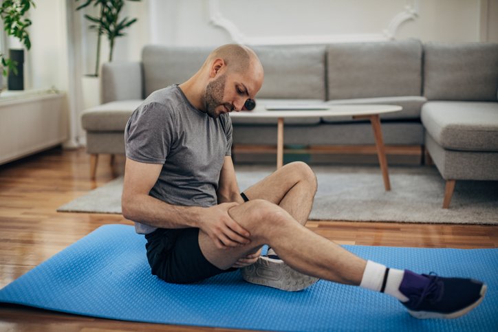 man holding leg sitting on yoga mat